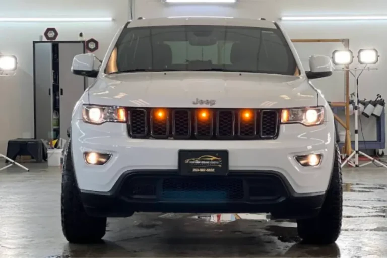 Front view of white Jeep with lights on in detailing bay