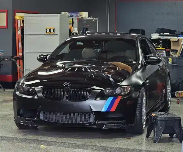 Black BMW coupe inside professional car detailing shop.