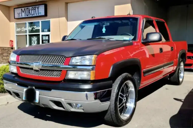 Front view of the red and black Chevrolet Silverado truck with shiny rims parked outside a building.